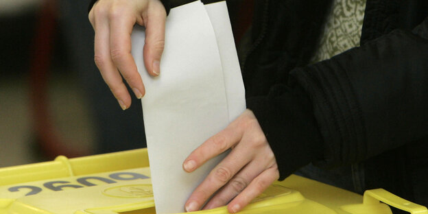Stimmzettel wird in eine Wahlurne gesteckt