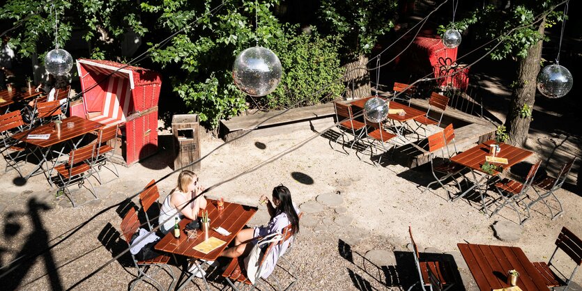 Zwei junge Frauen sitzen sich gegenüber in dem sonst leeren Biergarten