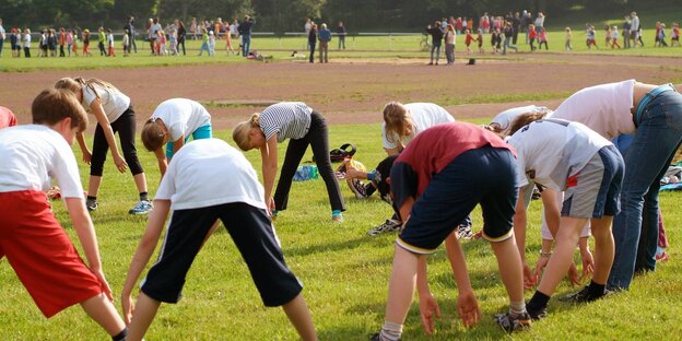 Kinder machen Dehnungsübungen auf einem großen Sportfeld