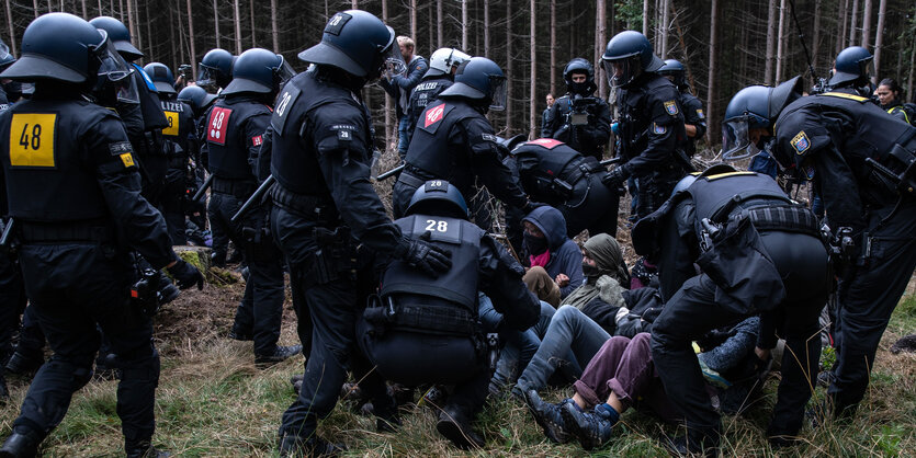 Ein Polizist steht im Wald vor einem Baum,haus der Demonstrant:innen