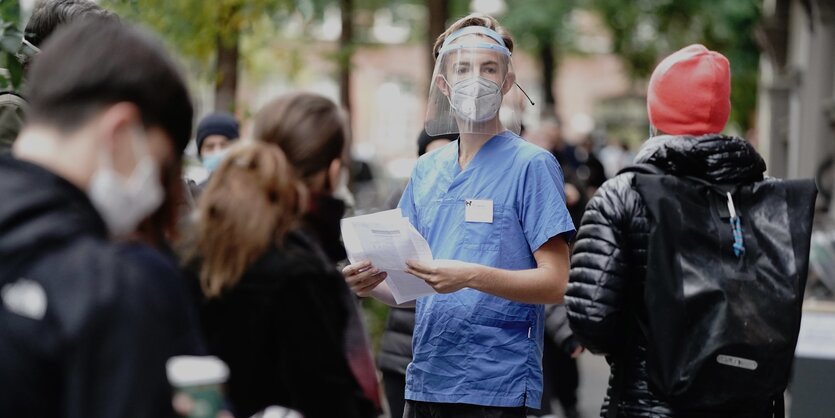 Medizinstudent Linus steht vor einer Arztpraxis im Bezirk Neukoelln bei wartenden Menschen, die für einen Corona-Test anstehen