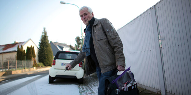 Mann mit Tasche und Autoschlüssel geht über eine verschneite Straße