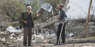 Zwei Männer in Berg-Karabach unterhalten sich vor einem zerbombten Haus.
