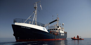 Das Seenotrettungsschiff Alan Kurdi im Meer. Ein kleines Schlauchboot schwimmt neben dem Schiff.