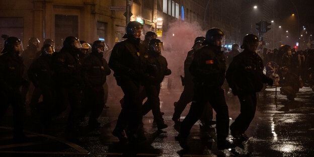Polizisten laufen bei einer Demonstration durch Rauch.