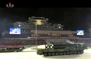 Bild des Staatsfernsehens von Nordkorea. eine große Parade mit vielen Menschen am Rand. Eine riesige, lange Rakete wird an den Menschen vorbeigezogen. Im Hintergrund ein Palast.