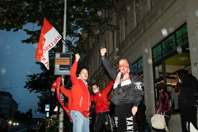 Drei Fussballfans mit Fahnen und Schals singen vor dem Kiez-Döner