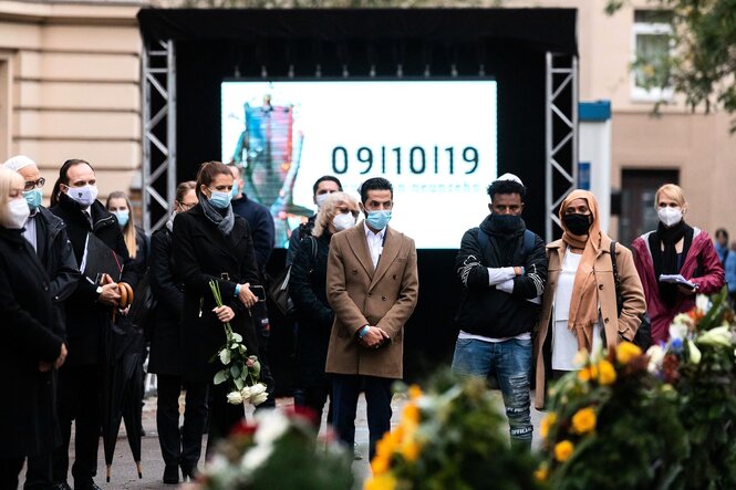 Menschen mit Masken sehen vor Kränzen und Blumengestecken