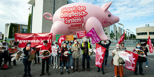 Demonstrant:innen mit Plakaten unter einem rosafarbenen aufblasbaren Schwein vor dem Bundeskanzleramt