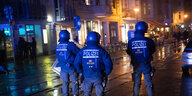 Polizisten in Schutzausrüstung stehen nachts auf einer regennassen Straße