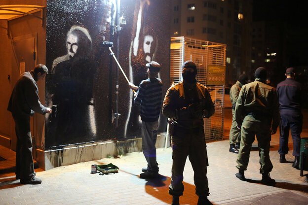 Eine Wandmalerei wird übermalt, während vermummte Polizisten die Arbeiten bewachen.