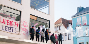 Hausbesetzer*innen stehen auf dem Balkon der Dete, Banner hängen an der Fassade