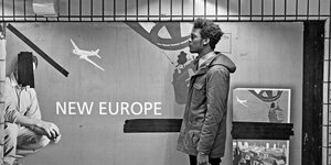 Vor dem Plakat einer Airline wartet ein junger Mann im Profil
