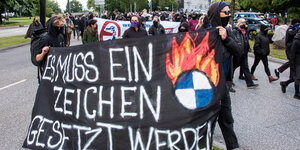 Vermummte Personen tragen ein Transparent mit einem brennenden BMW-Symbol