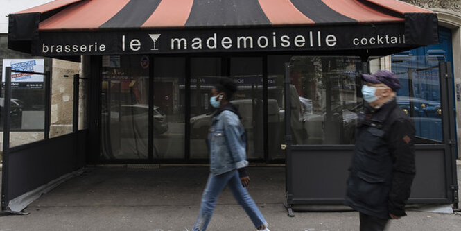 Menschen mit Maske laufen vor einer geschlossen Bar in Paris entlang