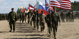 Nato-Soldaten verschiedener Nationen marschieren in einer Reihe mit Nationalfahnen