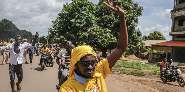 Eine Menschenmenge läuft eine Straße entlang, im Vordergrund hebt ein Mann in gelbem T-shirt seinen Arm