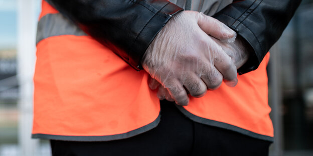Auschnitt zeigt Hände in Schutzhandschuhen und eine Warnweste.