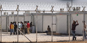 Abschiebegefängnis, Container hinter Stacheldrahtzaun, Häftlinge stehen in einer Gruppe im Hof