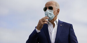 Joe Biden zupft an seiner Maske, im Hintergrund Himmel