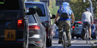 Zwei Fahradfahrende auf einer Radspur neben dichtem Autoverkehr