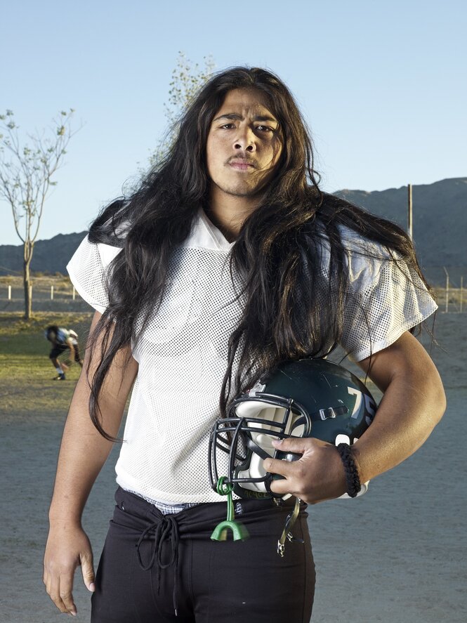 Farbfoto, junger Rugby-Spieler mit Helm im Arm und langen dunklen Haaren