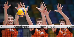 Drei Volleyballspieler blocken am Netz einen Ball