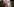 Vor einem Bus der Johanniter übergibt eine Frau eine Schale mit Essen. Im erleuchteten Inneren des Busses füllt ein Mann Schalen, Im vordergrund zwei dunkle Gestalten