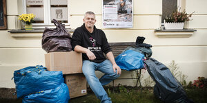 Andreas Steinert von Wir packens an sitzt vor der Spenden-Sammelstelle Frauenzentrum Paula Panke neben Kartons und Säcken mit Kleiderspenden