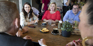 Ministerpräsidentin Jacinda Ardern sitzt mit mehreren Menschen beim Kuchen und lächelt