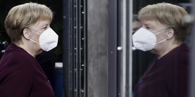 Kanzlerin Merkel mit Mund-Nasen-Schutz vor einem Spiegel stehend