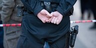 Ein Polizist steht hinter einer Polizeiabsperrung und hat die Hände hinter dem Rücken verschränkt