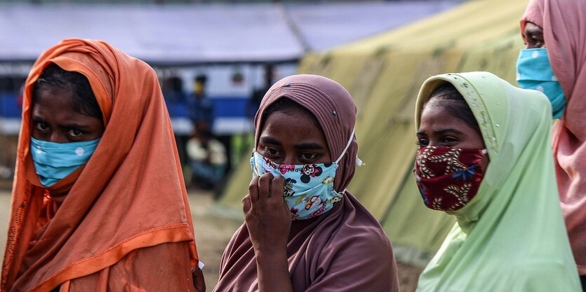 Drei Frauen mit bunten Kopftüchern und Gesichtsmasken in einer warteschlange