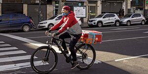 Mann mit unter der Nase getragener Alltagsmaske auf einem Fahrrad in verkehrsarmer Straße
