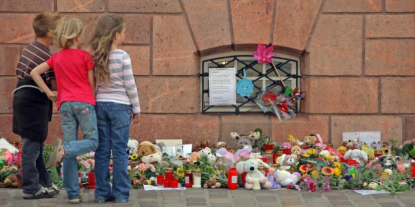 drei kinder stehen vor einem gedenkort mit blumen