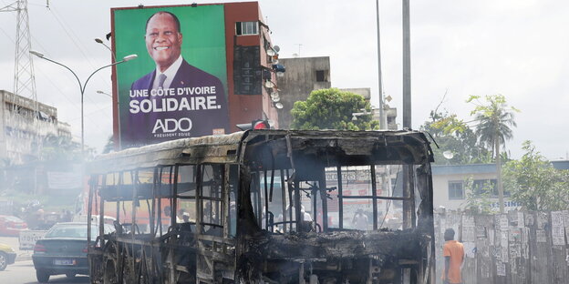 Eine Wahlplakat mit dem Konterfei des Präsidenten, davor ein ausgebrannter Bus