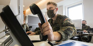 Ein Soldat greift den Hörer eines Telefons, er trägt Mundschutz
