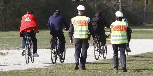Ein Streifenpolizist und eine Streifenpolizistein und drei Radfahrer im Englischen Garten in München