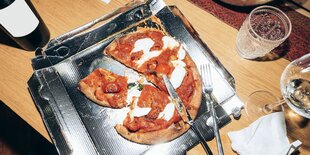 Auf einem unaufgeräumten Esstisch liegt eine halb aufgessene Pizza