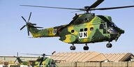 Zwei Militärhubschrauber auf dem Gelände einer Militär-Basis in Mali. Einer der Hubschrauber schwebt in der Luft, während der Zweite sich am Boden befindet