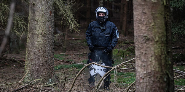 Ein Polizist mit Helm und in Uniform steht alleine zwischen Bäumen