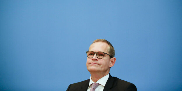Michael Müller sitzt vor einer blauen Wand auf einer Pressekonferenz