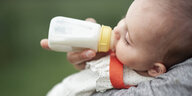 Eine Mutter hält ein Baby im Arm dass aus einer babyflasche trinkt