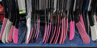 Das Bild zeigt viele Eishockeyschläger, deren Spitzen rosa gefärbt sind.