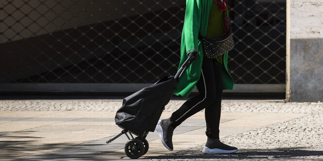 Frau läuft mit einem Einkaufstrolley auf einer Straße in Berlin.