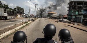 Drei Polizisten beobachten eine Rauchsäule in einer Straße con Conakry, der Hauptsadt von Guinea