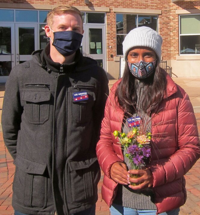 Lee Griffin und seine Frau schauen in die Kamera, er hat die Hände hinterm Rücken, sie Blumen in der Hand. Beide tragen Maske