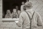 Eine junge Familie mit kleinen Kinder schaut zu einem Mann, der vor ihrem geöffneten Fenster steht