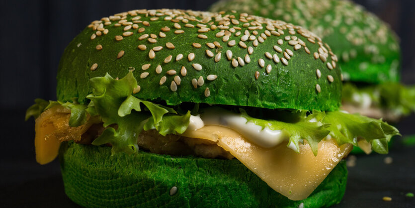 Ein gruen gefaerbter Burger mit Salat und Kaese liegt auf einem schwarzen Untergrund