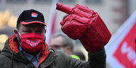 Ein Mann steht bei einer Kundgebung der Gewerkschaft verdi auf einem OPlatz. Er trägt einen Mundschutz und hebt seine Hand in die Luft. An der Hand: Ein riesiger Handschuh, der den Stinkefinger zeigt.
